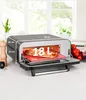 A countertop pizza oven with a pizza inside, on a kitchen counter, with some ingredients in the background. Anteprima dell’immagine prodotto