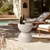 A modern outdoor patio setting with a pool and lounge chairs, featuring a speckled white side table with wine bottles and glasses. Podgląd zdjęcia produktu