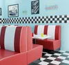 A retro diner booth setting with red and white striped seating, a checkerboard floor, and classic diner decor. Produktbild-Vorschau