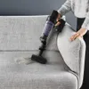 A person is using a cordless vacuum cleaner to clean a sofa. Náhled obrázku produktu