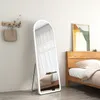 A full-length mirror with LED lighting is placed in a bedroom next to a wooden bed.