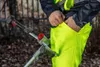 A person wearing high-visibility work pants and jacket, with a tool in the background. Produktbild-Vorschau