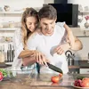 A couple is preparing food in a kitchen. The man is cutting a tomato on a cutting board, and the woman is embracing him from behind. Produktbild-Vorschau