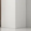 A close-up view of the corner of a white cabinet against a light gray wall and a reflective floor. Náhled obrázku produktu