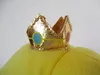 A close-up of a golden crown with blue and pink jewels on top of a yellow plush toy. Náhľad obrázku produktu