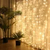 A curtain of warm white LED string lights hangs behind two potted plants, creating a festive and cozy atmosphere. Produktbild-Vorschau