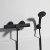 A black shower thermostat and shower head mounted on a white wall. Anteprima dell’immagine prodotto