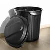 A black trash can with its lid open, placed on a wooden floor next to a white wall. Podgląd zdjęcia produktu