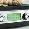 A close-up view of a digital display on a grill, showing cooking times and temperatures for the upper and lower plates, with food visible in the background. Produktbild-Vorschau