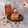 A hand drizzling honey onto waffles from a honey dipper, with a jar of honey and nuts in the background. Produktbild-Vorschau