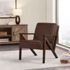 A dark brown faux leather armchair with wooden legs is placed on a light-colored rug in a living room setting. A wooden cabinet with a lamp and decorative items is visible in the background, along with a large window. Produktbild-Vorschau