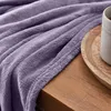 A close-up of a purple blanket draped over a wooden surface, with a mug on a wooden tray in the background. Anteprima dell’immagine prodotto