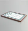 A framed certificate is shown at an angle on a plain gray surface. Produktbild-Vorschau