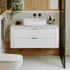 A modern bathroom vanity with a white countertop sink and a white cabinet with ribbed drawers, set against a light-colored wall and wood accents. Náhled obrázku produktu