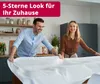 A couple is setting a table with a white tablecloth in a kitchen. Produktbild-Vorschau