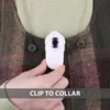A hand holds a small white camera near the collar of a plaid shirt. Náhled obrázku produktu