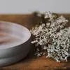 A close-up shot of a light gray ceramic bowl and a bunch of small white flowers on a wooden surface. Produktbild-Vorschau