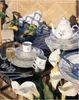 A table setting with a teapot, cups, plates, and glasses, decorated with flowers and lemons. Produktbild-Vorschau
