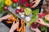 A top-down view of hands preparing vegetables on a wooden table. Náhľad obrázku produktu
