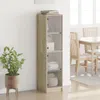 A tall, narrow cabinet with glass doors stands against a white wall, next to a potted plant. A dining table and chairs are visible in the background. Anteprima dell’immagine prodotto