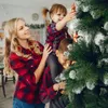 A mother and her two children are decorating a Christmas tree. The mother is holding her daughter on her shoulders, and her son is standing next to them, holding onto the tree. Podgląd zdjęcia produktu