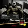 A muscular bodybuilder poses in a gym setting with dumbbells and a tub of Activlab Creatine Monohydrate. Náhled obrázku produktu