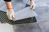 A person wearing gloves is laying a tile onto a floor with adhesive. Produktbild-Vorschau