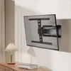 A TV wall mount is shown attached to a television on a wall, with a lamp and books on a wooden dresser in the foreground. Podgląd zdjęcia produktu