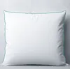 A white pillow with a teal trim is shown against a light gray wall. Produktbild-Vorschau
