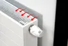 A white radiator with a white thermostat and red arrows indicating heat flow, placed against a wall with a reflective insulation sheet. Podgląd zdjęcia produktu