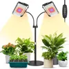 A grow light stand with two adjustable lamps illuminates several potted plants and a seedling tray. Náhled obrázku produktu