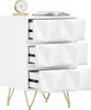A white nightstand with three drawers and gold legs, shown from a slightly diagonal front view. A clock and a book are on top. Produktbild-Vorschau
