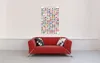 A red sofa with two pillows in front of a white wall, with a poster of flags on the wall. Náhled obrázku produktu