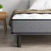 A close-up view of a mattress and bed frame, with a bedside table and a plant in the background. Voir les images du produit