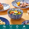 A collection of blue and white patterned tableware, including plates and bowls, filled with food, set on a wooden table. Produktbild-Vorschau