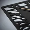 A close-up, angled view of a modern, black wall clock with a geometric cutout design and a thin gold hand. Anteprima dell’immagine prodotto