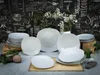 A collection of white ceramic plates and bowls arranged on a table in front of a chalkboard-style background with decorative text and flowers. Náhľad obrázku produktu