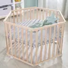 A hexagonal wooden playpen with a gray patterned mat and a green blanket and star-shaped pillow inside. Produktbild-Vorschau