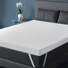 A white mattress topper is shown on a bed with gray pillows and a gray headboard, against a blue wall. Produktbild-Vorschau