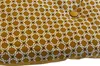 A close-up view of a mustard yellow cushion with a repeating white and black geometric pattern. A single button is visible on the cushion. Náhled obrázku produktu