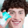 A close-up shot of a young man holding a teal and white product pouch near his eye. Produktbild-Vorschau