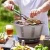 A person is grilling food on a portable electric grill outdoors, with a mug of beer and vegetables on the table. Produktbild-Vorschau