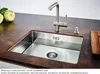 A stainless steel kitchen sink with a faucet and soap dispenser on a dark brown countertop, with two kohlrabi vegetables in the background. Náhled obrázku produktu