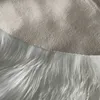 A close-up view of the edge of a white faux fur rug meeting a beige fabric. Náhľad obrázku produktu
