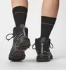 A close-up view of a person's legs wearing black Salomon hiking socks and black Salomon hiking boots. Produktbild-Vorschau