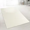 A cream-colored shaggy rug is laid out on a light wooden floor in a brightly lit room with sheer curtains in the background. Produktbild-Vorschau