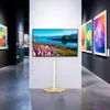 A TV stand with a landscape image displayed on the screen, set in a modern art gallery. Produktbild-Vorschau
