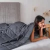 A woman is lying on a bed under a weighted blanket. Produktbild-Vorschau