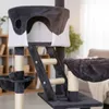 A close-up view of a multi-level cat tree with various platforms, scratching posts, and a hammock, set in a home environment with blurred background elements. Produktbild-Vorschau