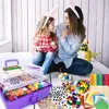 A mother and daughter are sitting on the floor, engaged in an Easter craft activity. They are both wearing bunny ears and appear to be decorating eggs. A large craft supply box is open in the foreground, filled with various art and craft materials. Produktbild-Vorschau